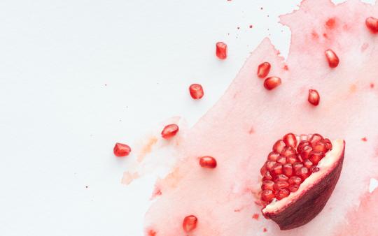 A pomegranate quarter spilling pips onto a white surface, their juices pooled.