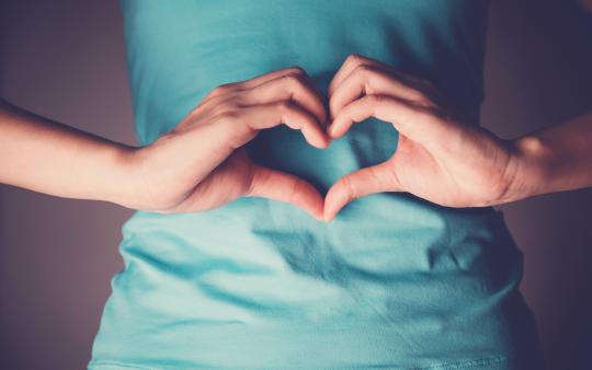 A woman makes a heart with her hands over her stomach