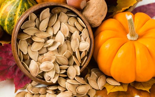 pumpkin seeds fall out of a basket beside a small pumpkin