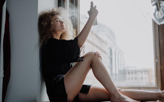 a woman sits on the floor and uses a face mist