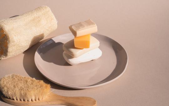 A stack of soap bars on a plate next to a scrub brush and towel