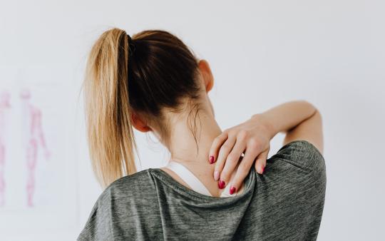 a woman facing away from the camera touching her neck 