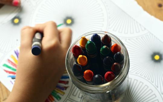 person colouring a picture with crayons with a jar of crayons next to them