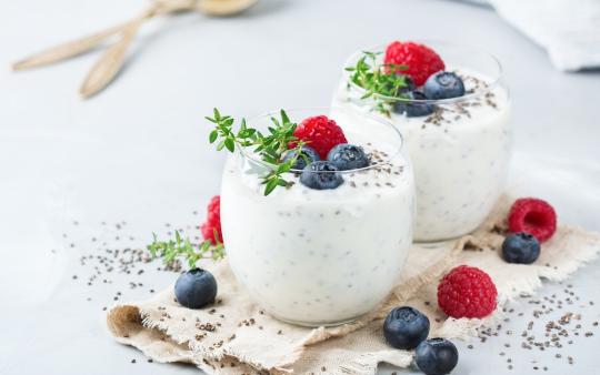 two glasses with chia-berry pudding in them with berries on top and beside the glasses