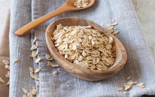 a wooden spoon and wooden bowl with oats in it