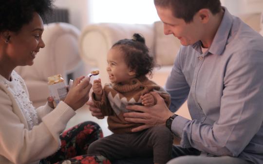 mother feeding toddler while father is holding the toddler