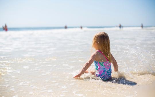 little girl in a bathing suit sitting on the beach in the water