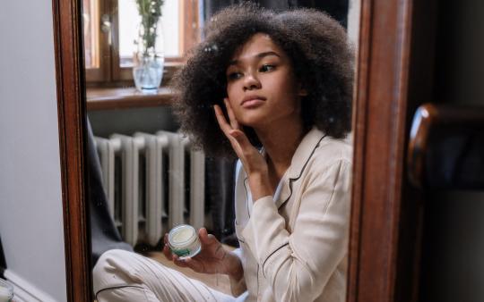 woman putting on moisturizer while looking in a mirror