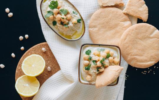 two pita breads and two bowls of hummus next to a halved lemon