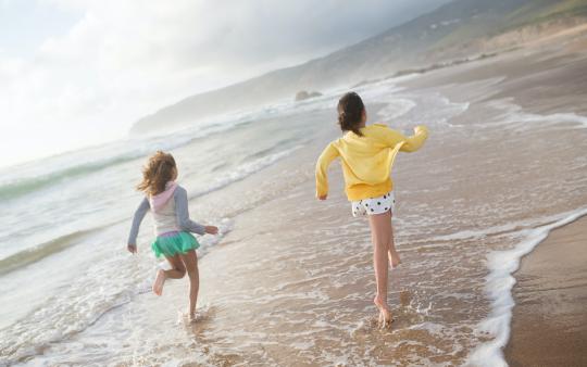 two kids run through the water across a beach's shoreline