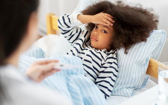 A parent checks a child's temperature while they lie in bed