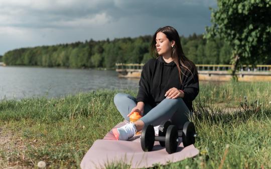 a woman sits outside in the grass with some workout equipment