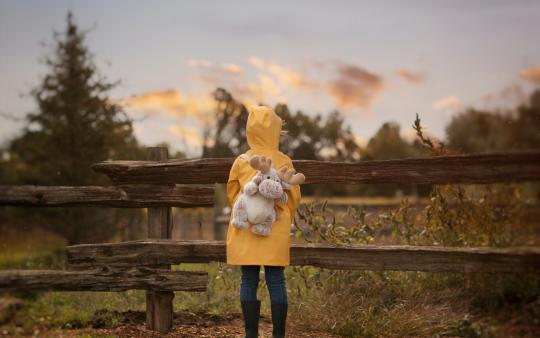 A child in raincoat looks over a wooden fence 