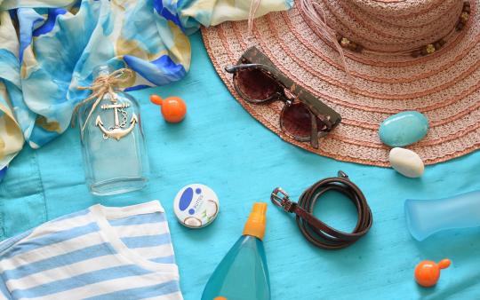 beach day accessories on a towel including lotion, a hat, and sunglasses