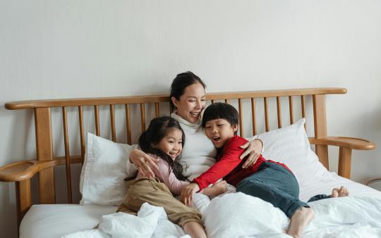 A mother and children laugh and cuddle in bed