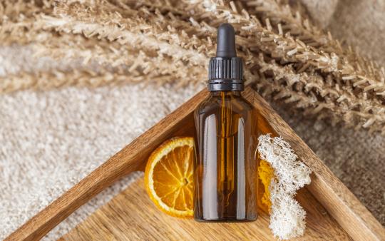 a skincare bottle in a wooden tray in front of an orange slice