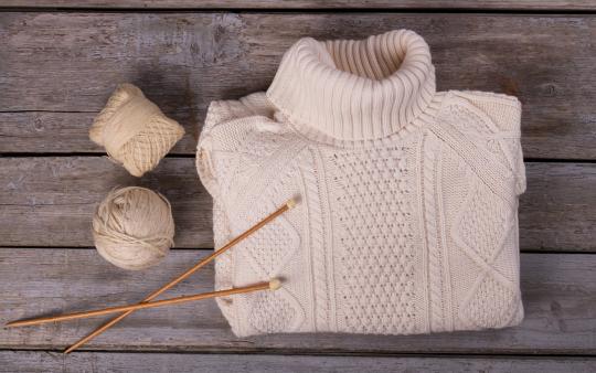 a folded knit sweater with yarn and knitting needles