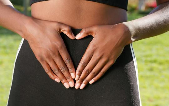 A woman makes a heart shape with her hands over her stomach