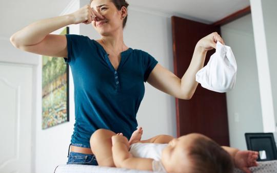 woman changing baby's diaper and plugging her nose