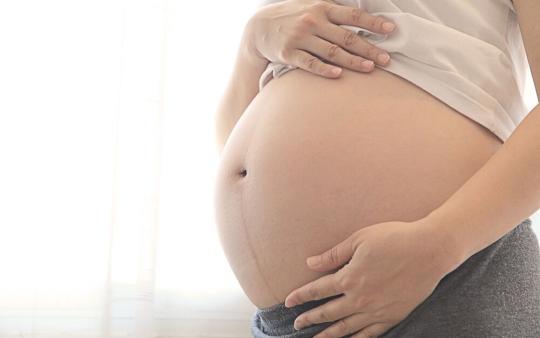 woman holding her bare, very pregnant abdomen