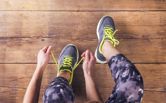 legs of woman in workout clothing tying her running shoes