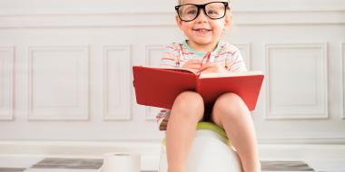 small child sitting on the potty and smiling with a red book on lap