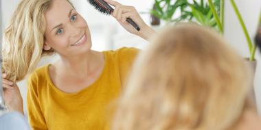 Woman brushing her long blonde hair while wearing a yellow top