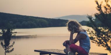 Child on a dock in summer, facing away from the camera with their head in their hand