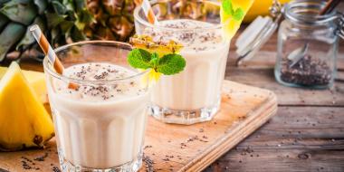 Two glasses filled with a beige beverage garnished with pineapple