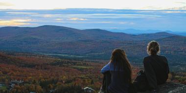 two teens sit and admire a view of trees below