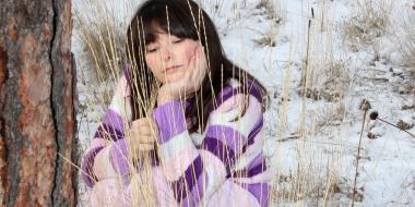 a woman sits in a wintry landscape and looks thoughtfully at a patch of grass 