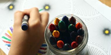 person colouring a picture with crayons with a jar of crayons next to them