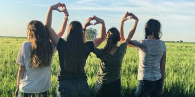 four teens face a field and link arms and hands to form heart shapes in the air