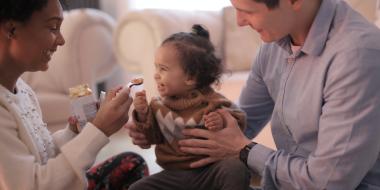 mother feeding toddler while father is holding the toddler