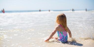 little girl in a bathing suit sitting on the beach in the water