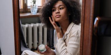 woman putting on moisturizer while looking in a mirror