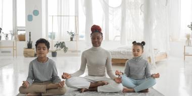 a mom and two kids meditating crosslegged on a yoga mat