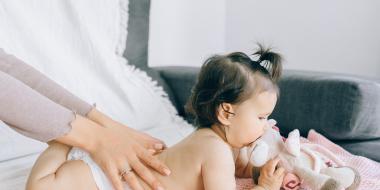 parent massaging back of infant with infant laying on stomach chewing toy