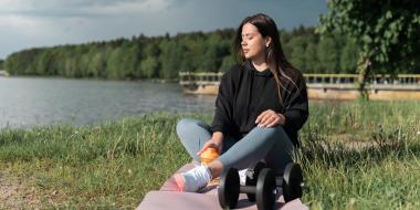 a woman sits outside in the grass with some workout equipment