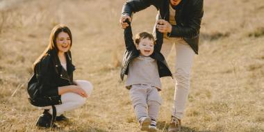 a father holds his toddler to help them kick a soccer ball