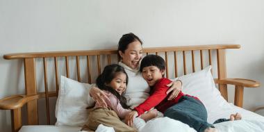 A mother and children laugh and cuddle in bed