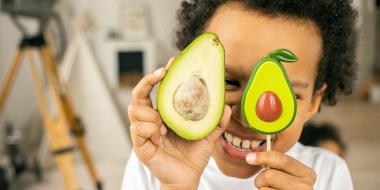 A concept photo of a child holding up two avocado halves