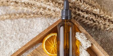 a skincare bottle in a wooden tray in front of an orange slice